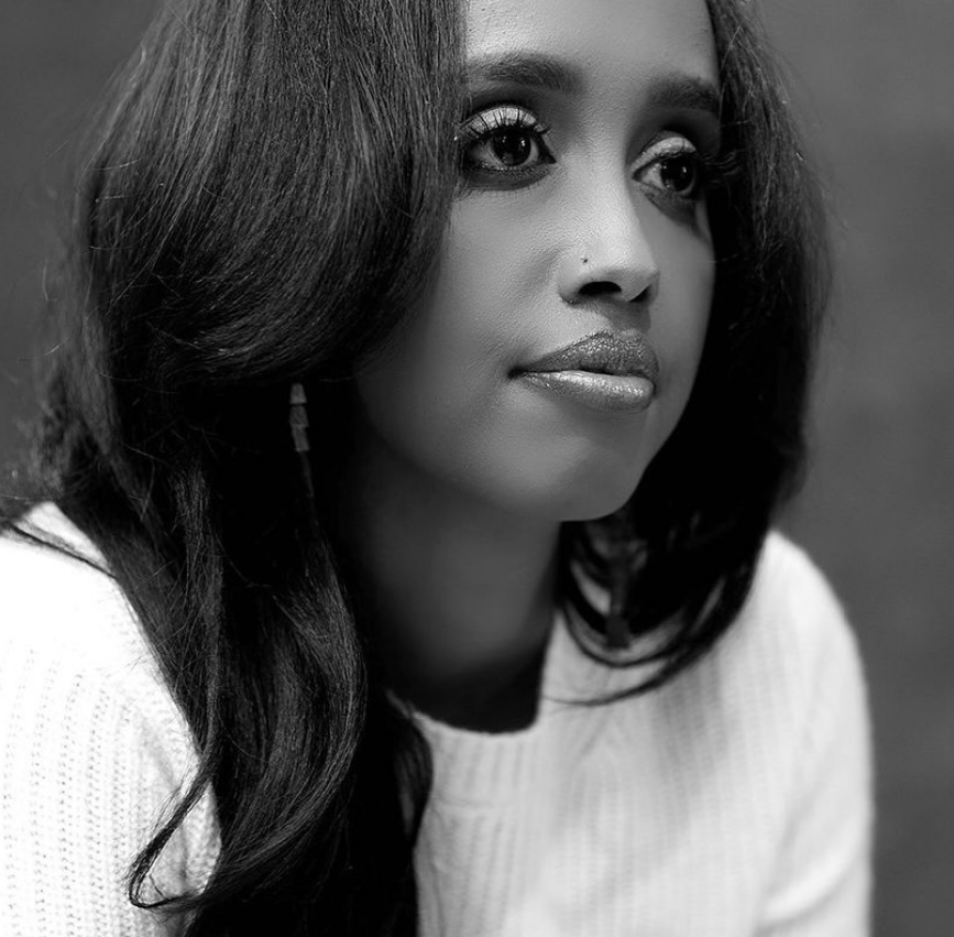 Black and white portrait of Neima Abdulahi with long hair, wearing a white sweater, looking to the side with a neutral expression.